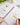 Person drawing flowers in a notebook with a paintbrush, surrounded by art supplies on a white surface.