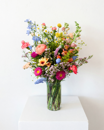 Bouquet of colorful flowers in a clear vase on a white surface with a white background