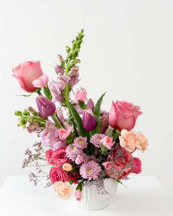 Bouquet of pink and purple flowers in a white vase on a white surface with a white background